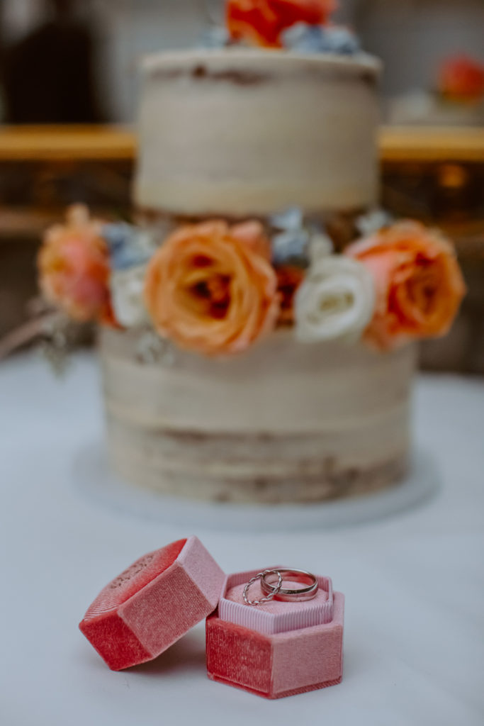 Detail photo of wedding rings with wedding cake in the background