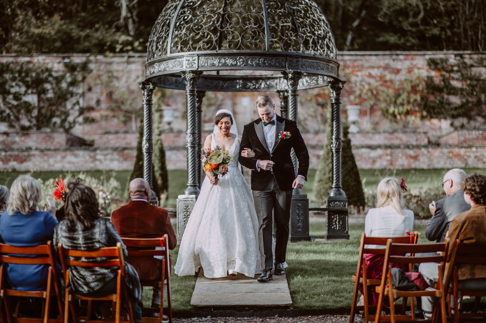 Happy couple smiling and walking down the isle together in walled garden after the ceremony. Beautiful Garthmyl Hall wedding photography