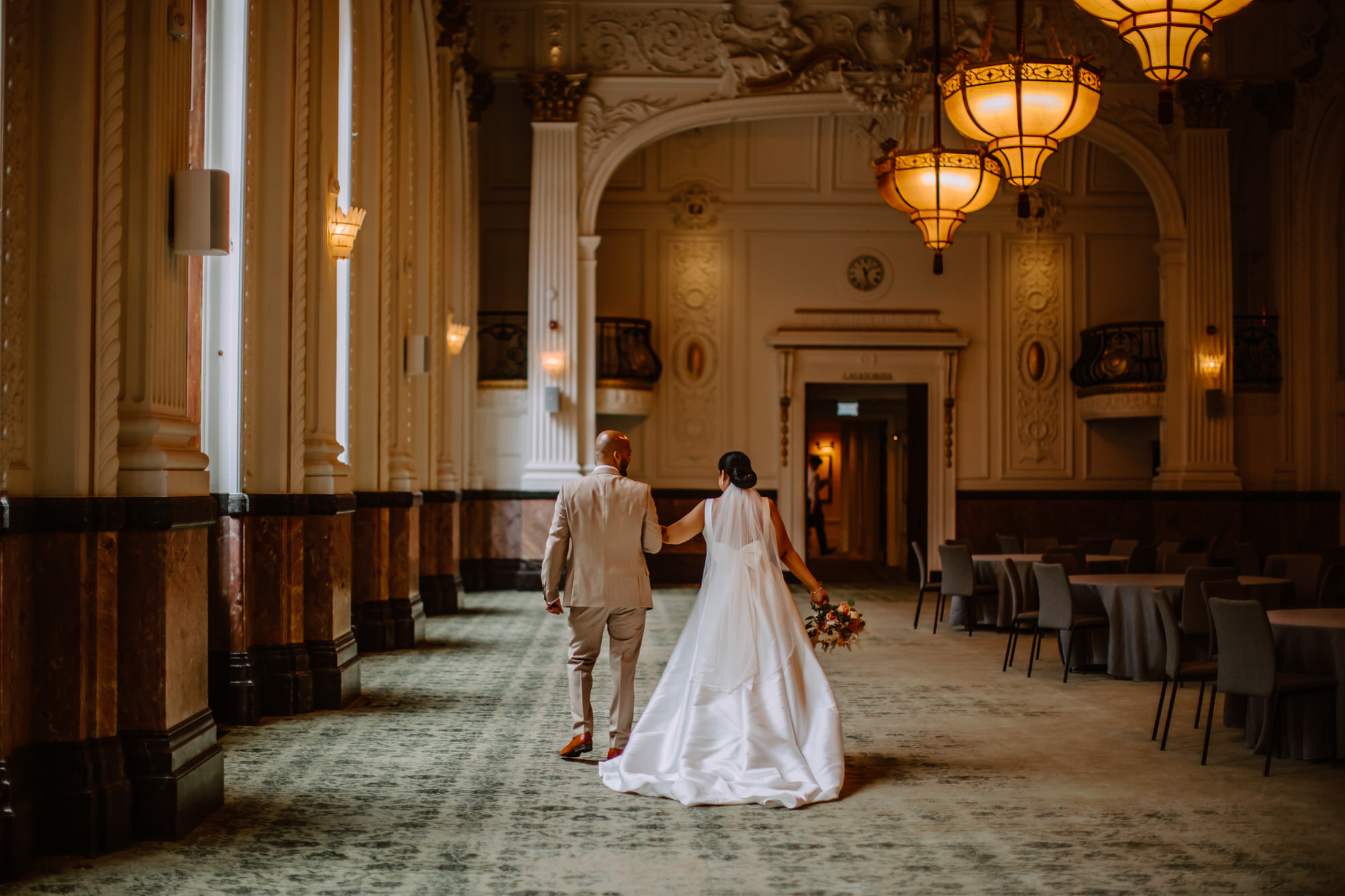 Bride and groom holding hands walking away in stunning Ballroom 