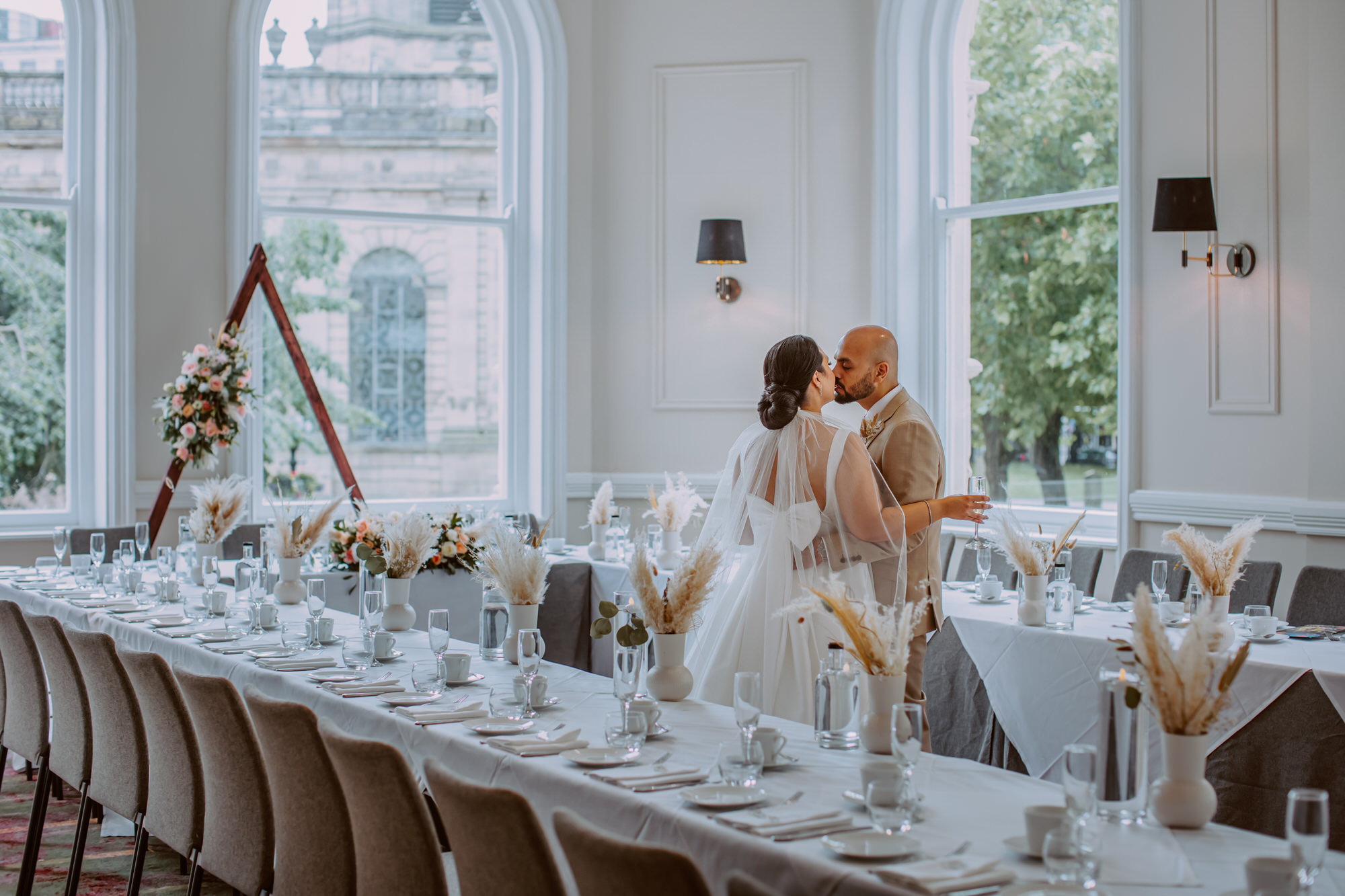 Bride and groom kiss while admiring the wedding breakfast table decoration