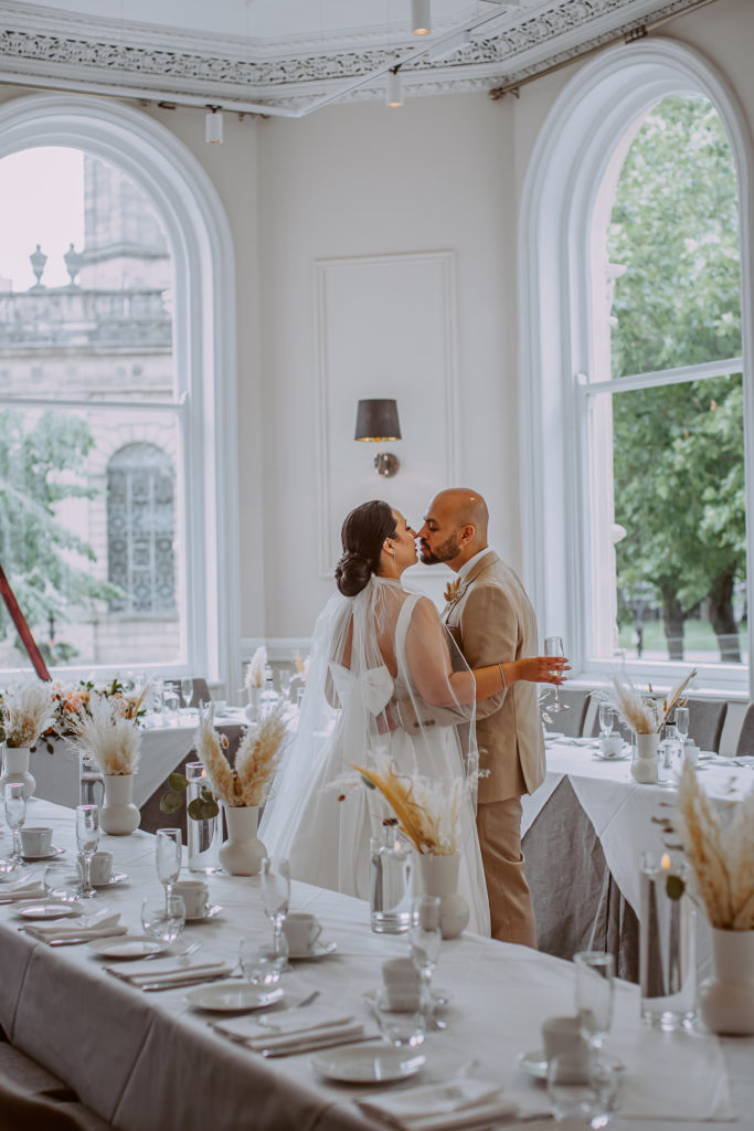 Bride and groom kiss while admiring the wedding breakfast decoration