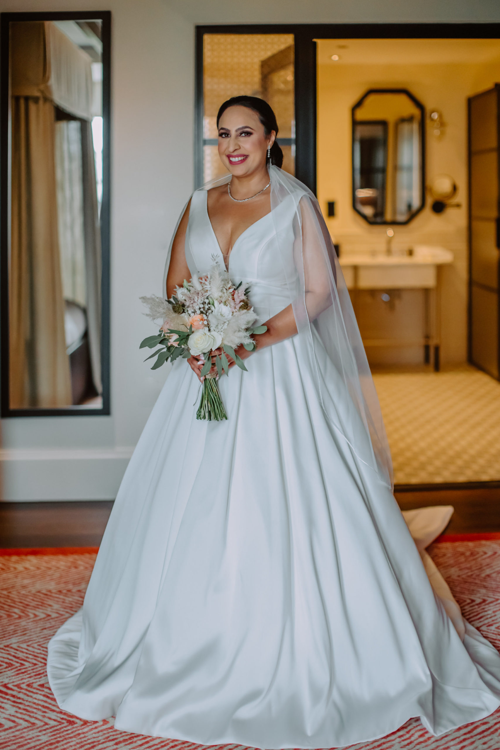 Bride smiling and looking into the camera in penthouse suite with beautiful bathroom in the background