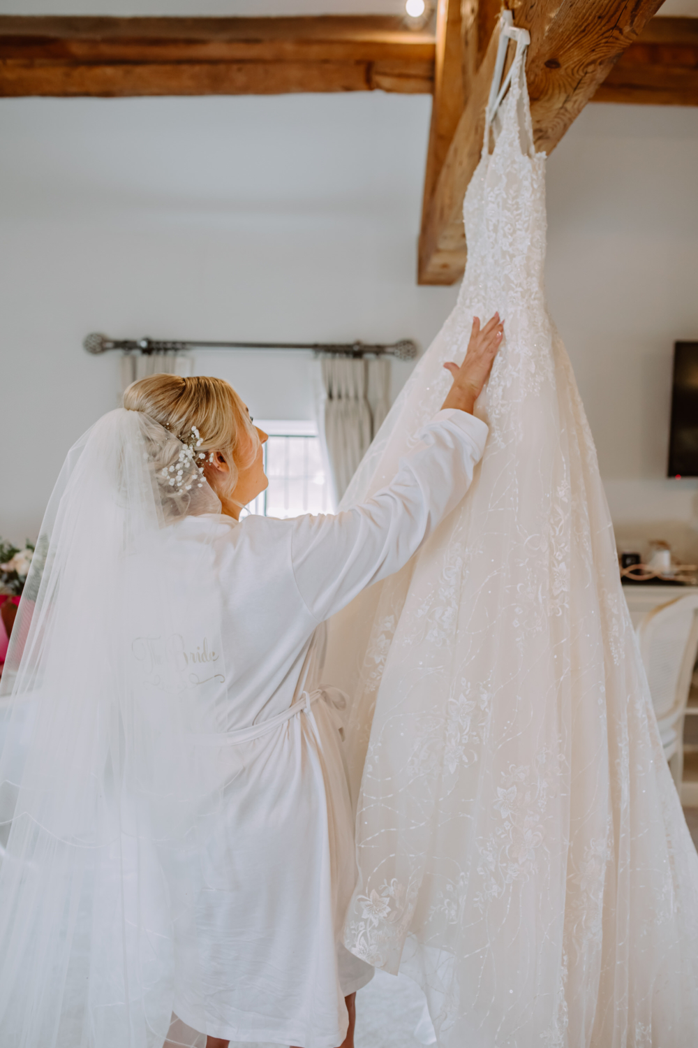 Bride admiring her dress hanging from the beam 