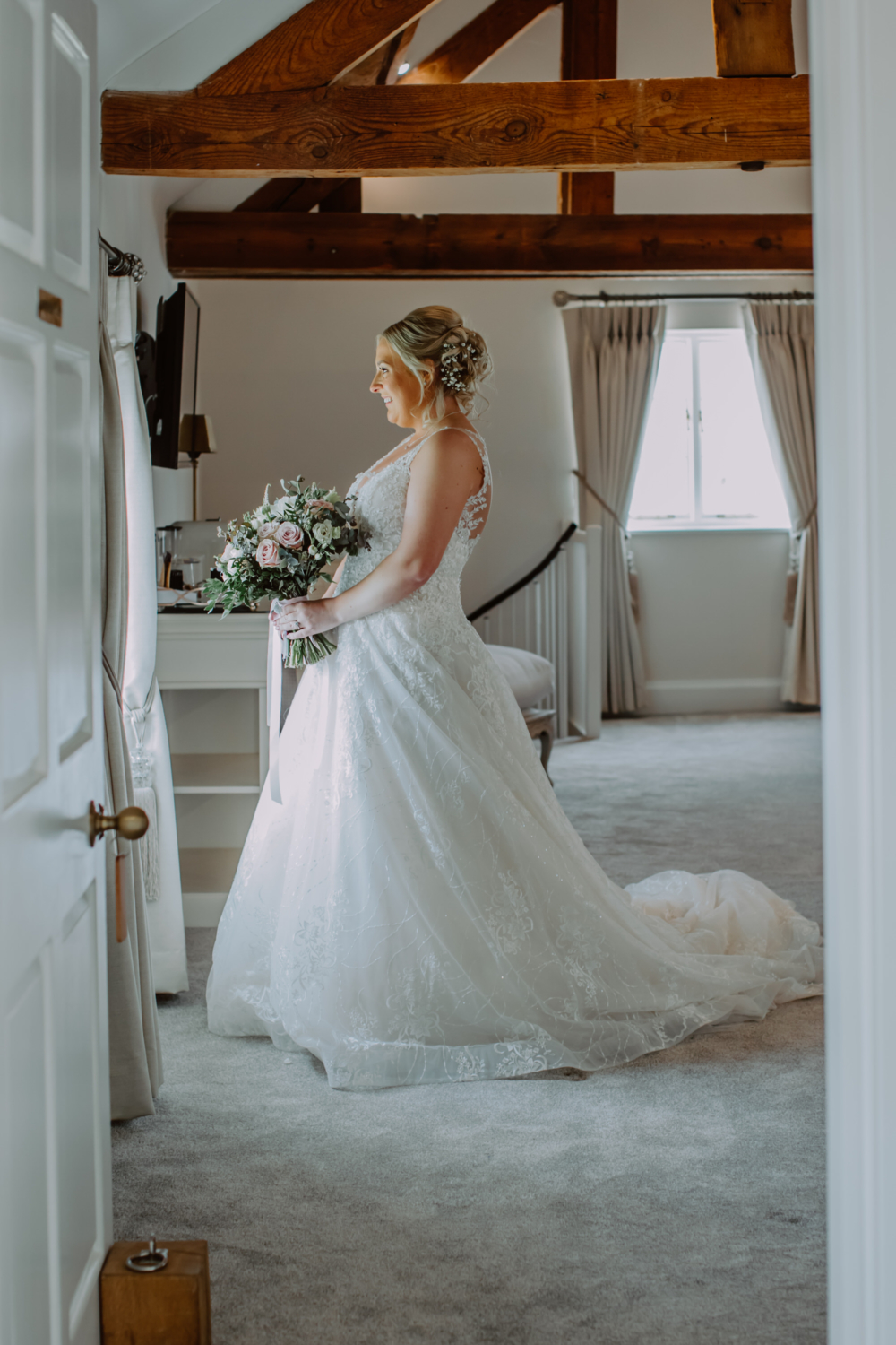 Full length photo of the bride holding her bouquet looking out the window 