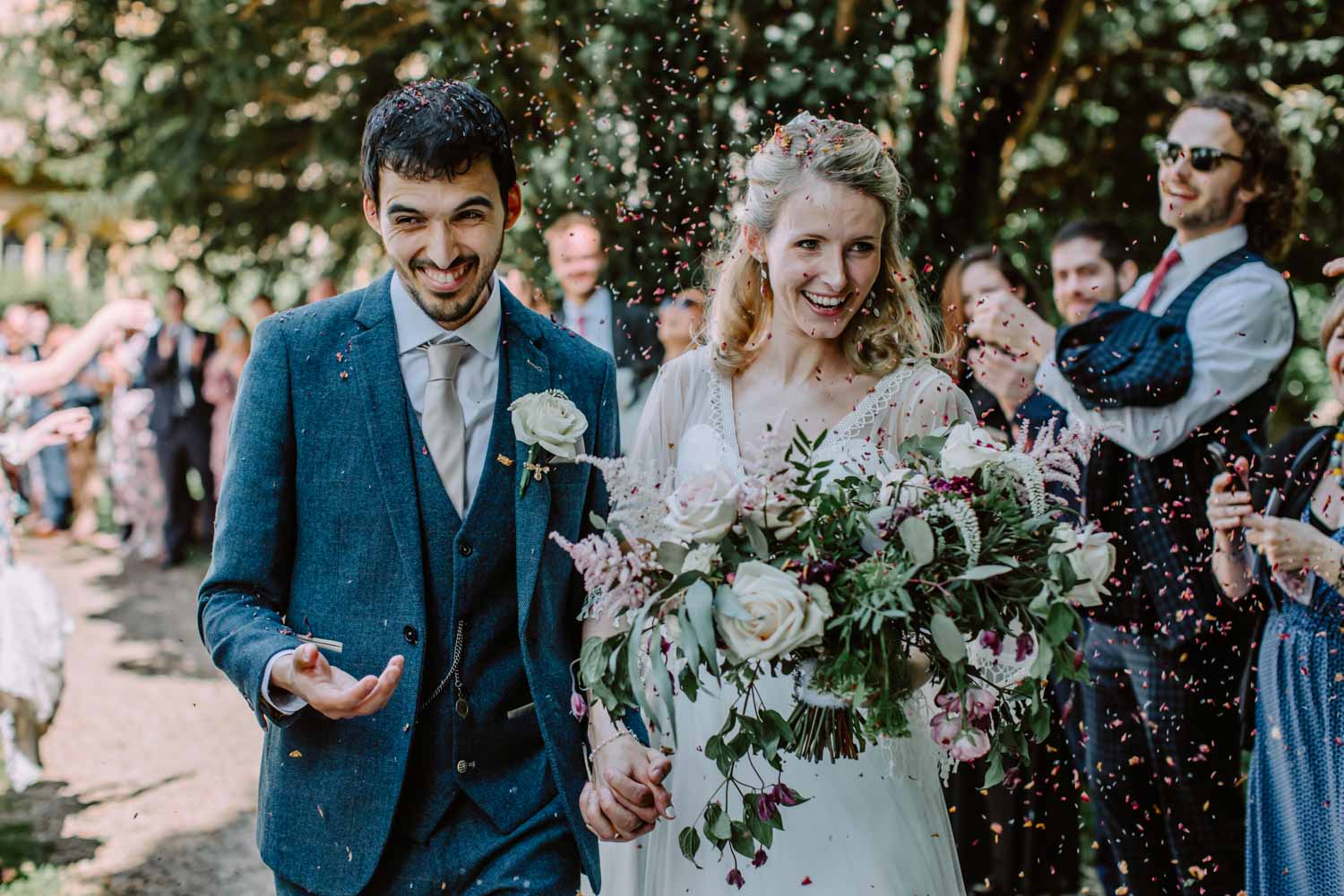Bride and groom smile while guests throw confetti 