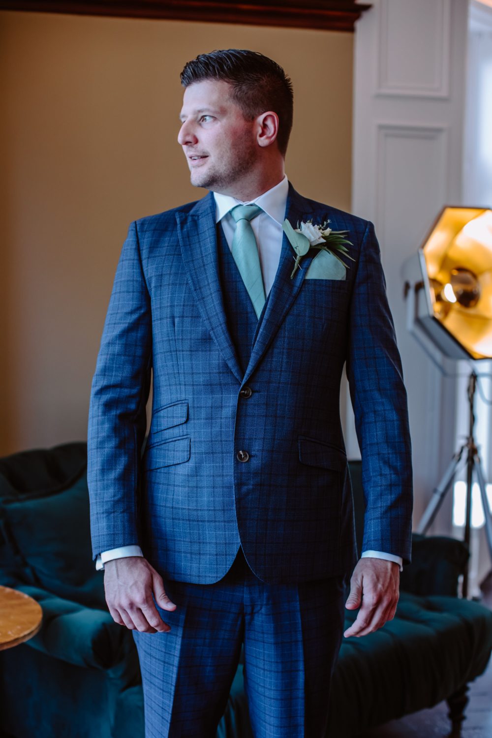 Groom dressed in the suit posing for the portrait looking out the window