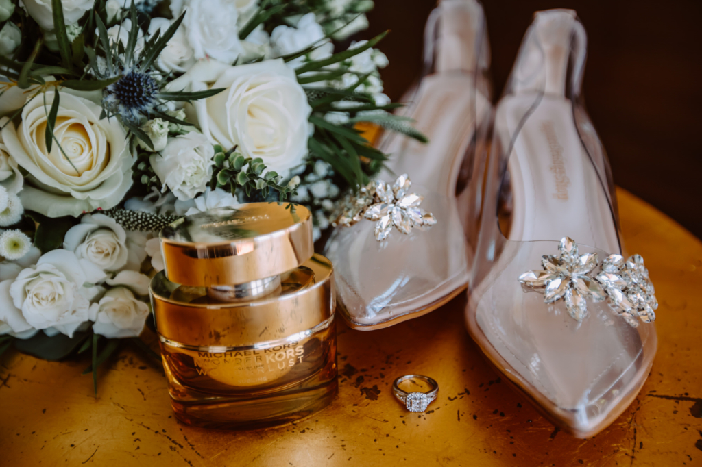 Detailed photo of bride's shoes, perfume, engagement ring and bouquet