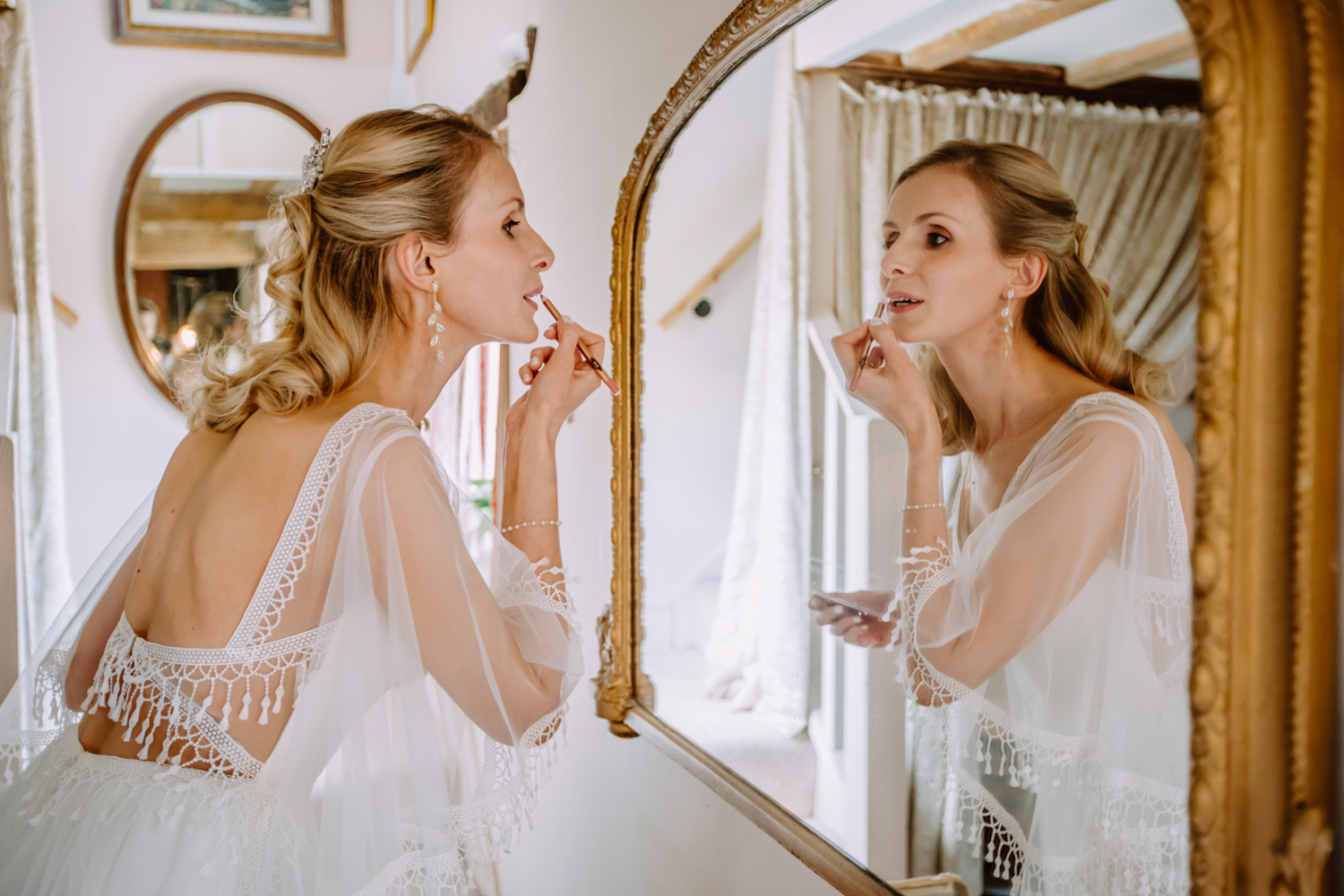 The bride applies the lipstick while looking into the mirror 