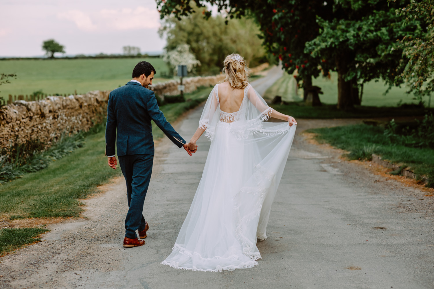 Wedding couple holds hands while walking away surrounded by the beautiful countryside