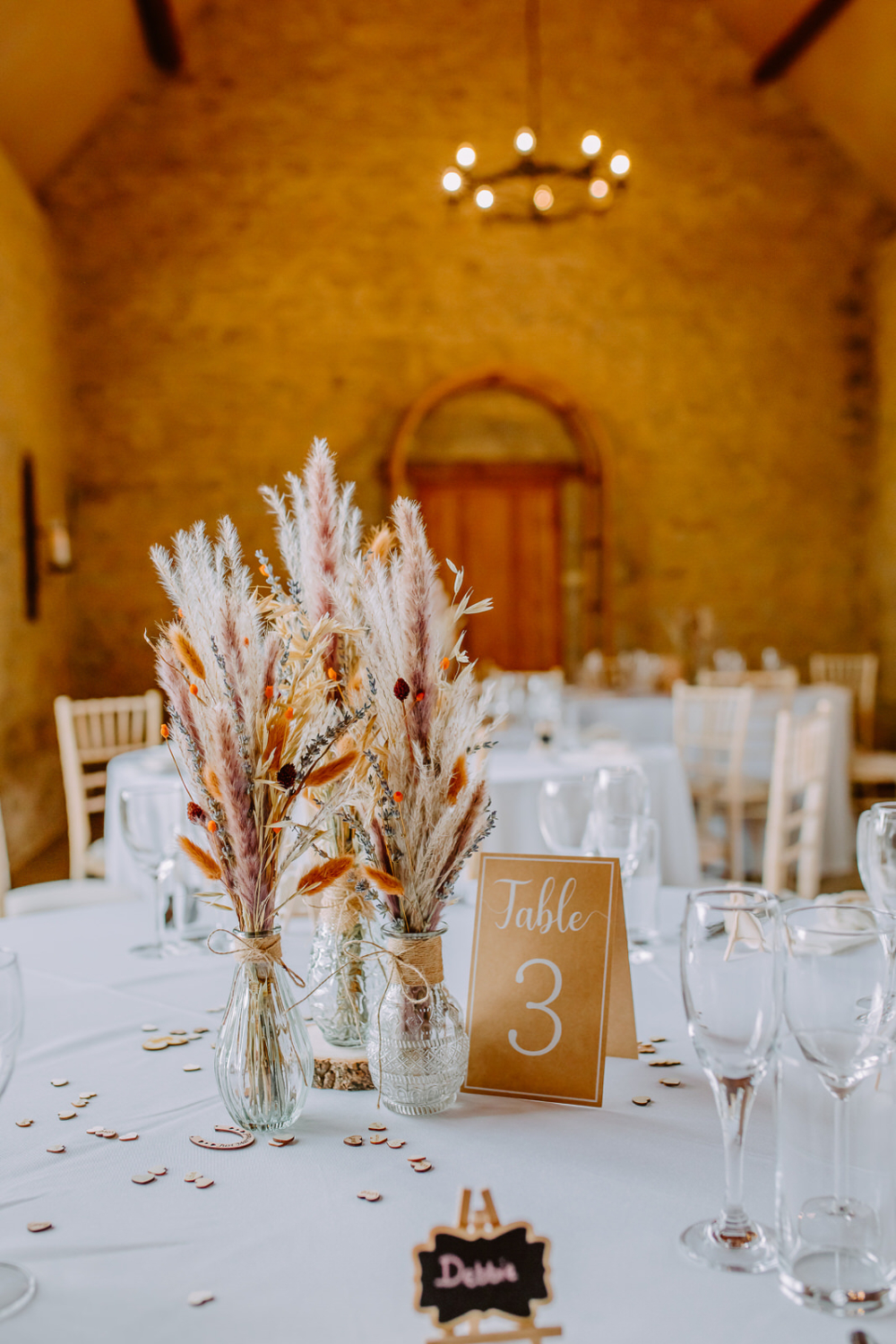Beautiful dried flowers in vase on the wedding breakfast table with a beautifully set up wedding breakfast room in the background. 