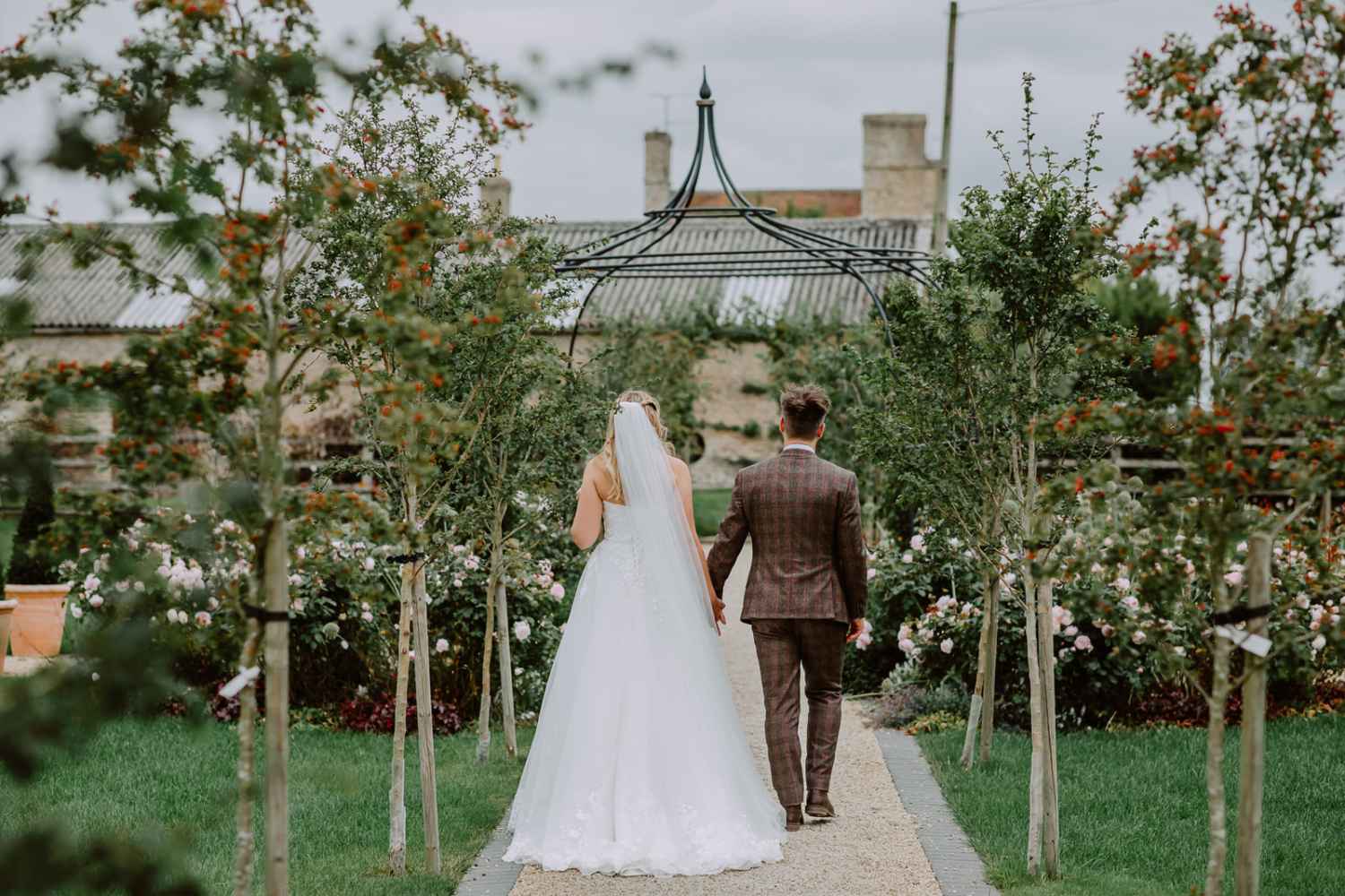 The wedding couple walks away through the Stratton court Barn formal rose gardens.