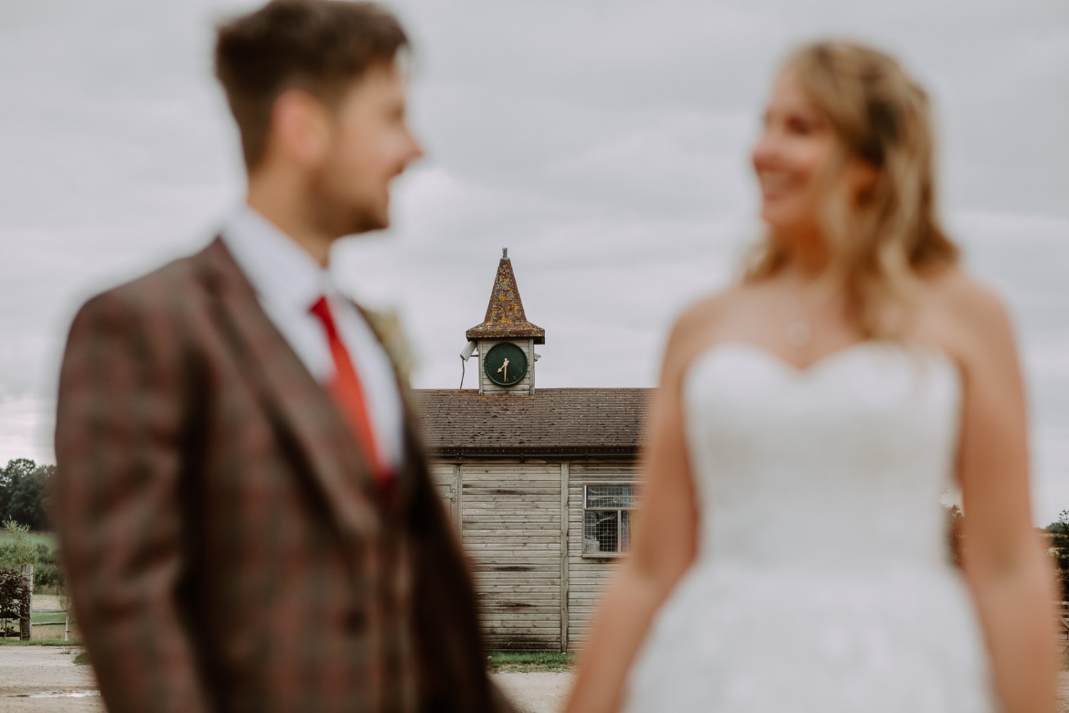 Detailed photo of the clock on the top of the barn with the couple out of the focus placed close to the camera