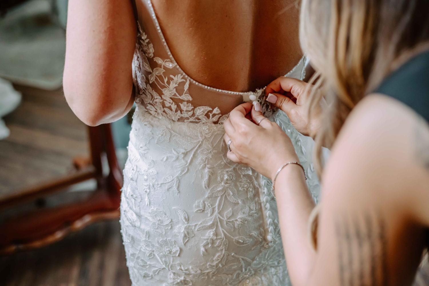 Maid of honor assisting bride in buttoning up her wedding dress.