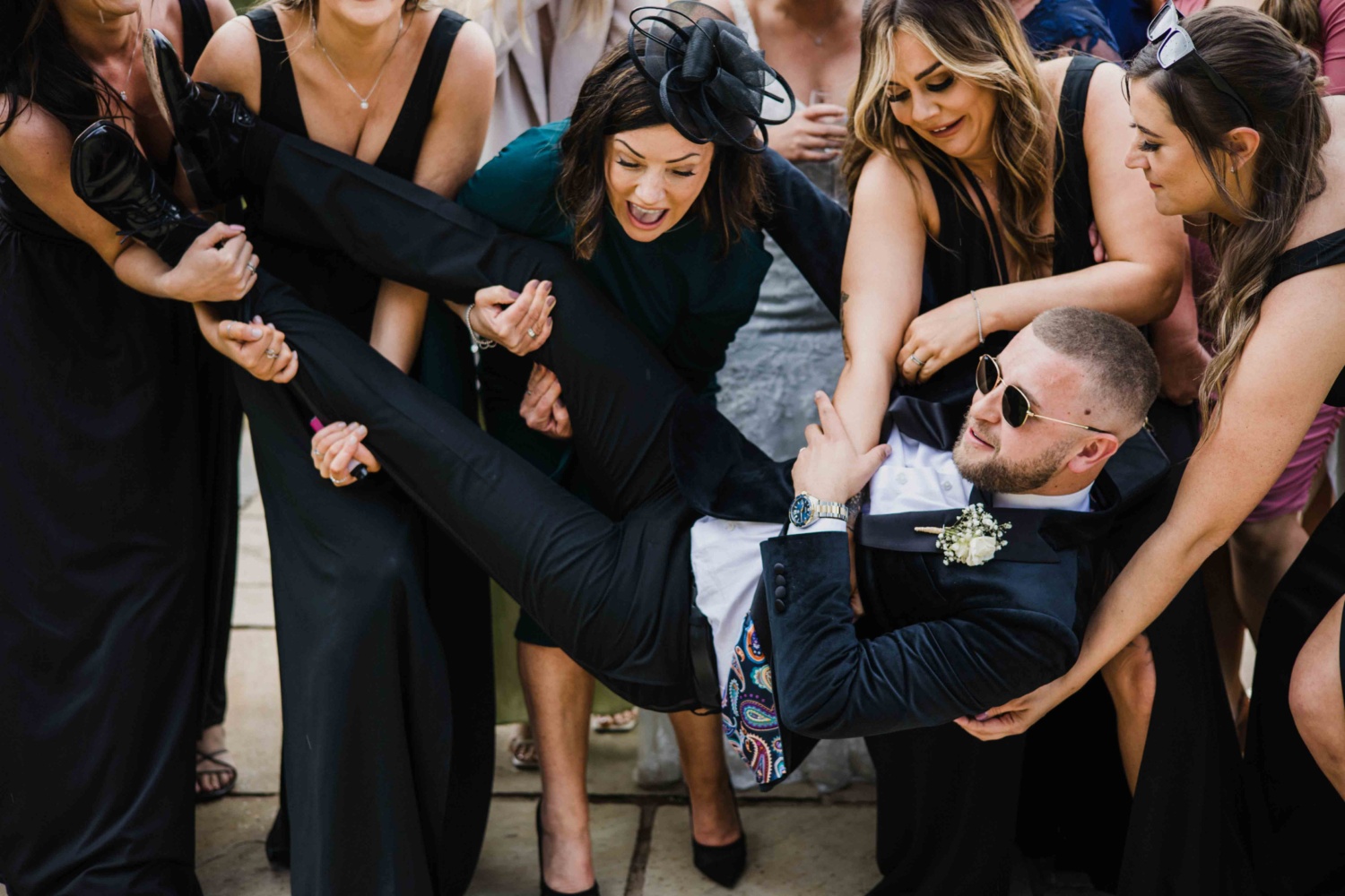 Women attempting to lift the groom in a playful moment.