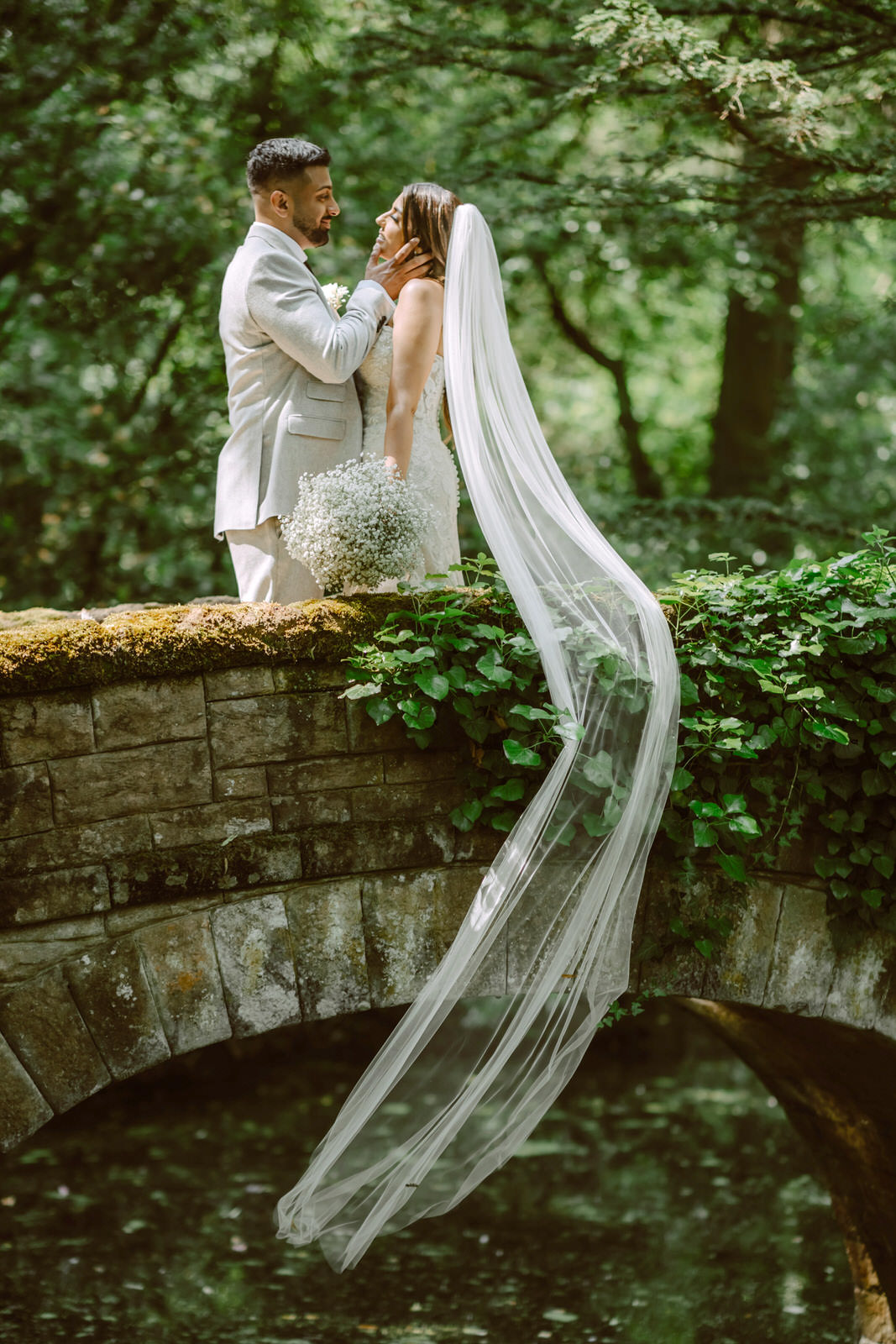 A bride and groom kissing on a bridge in the woods.
