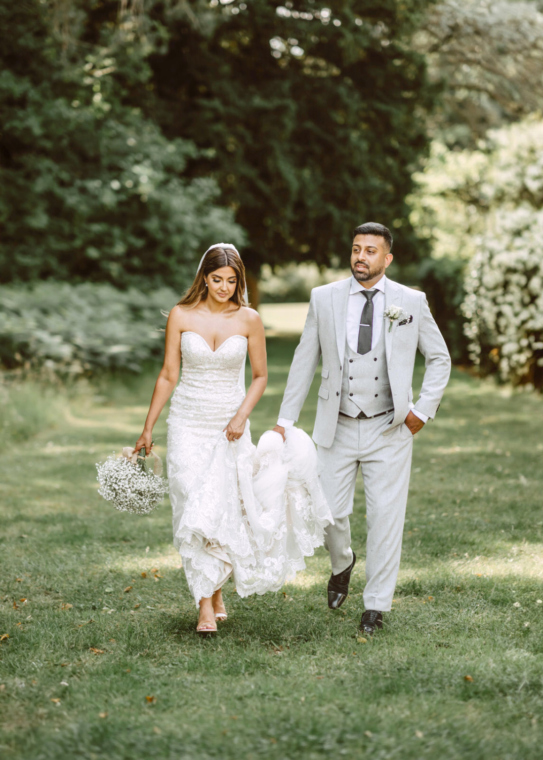 A bride and groom walking through a garden.