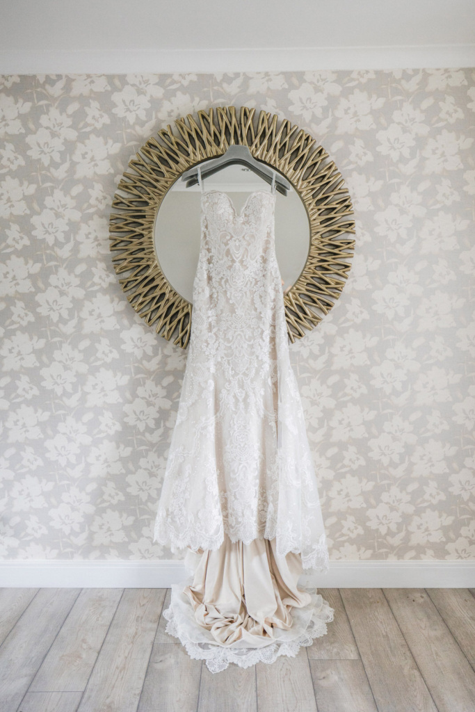 A wedding dress hangs in front of a mirror.