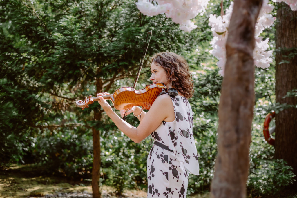 A woman playing a violin in a garden under cherry blossoms.