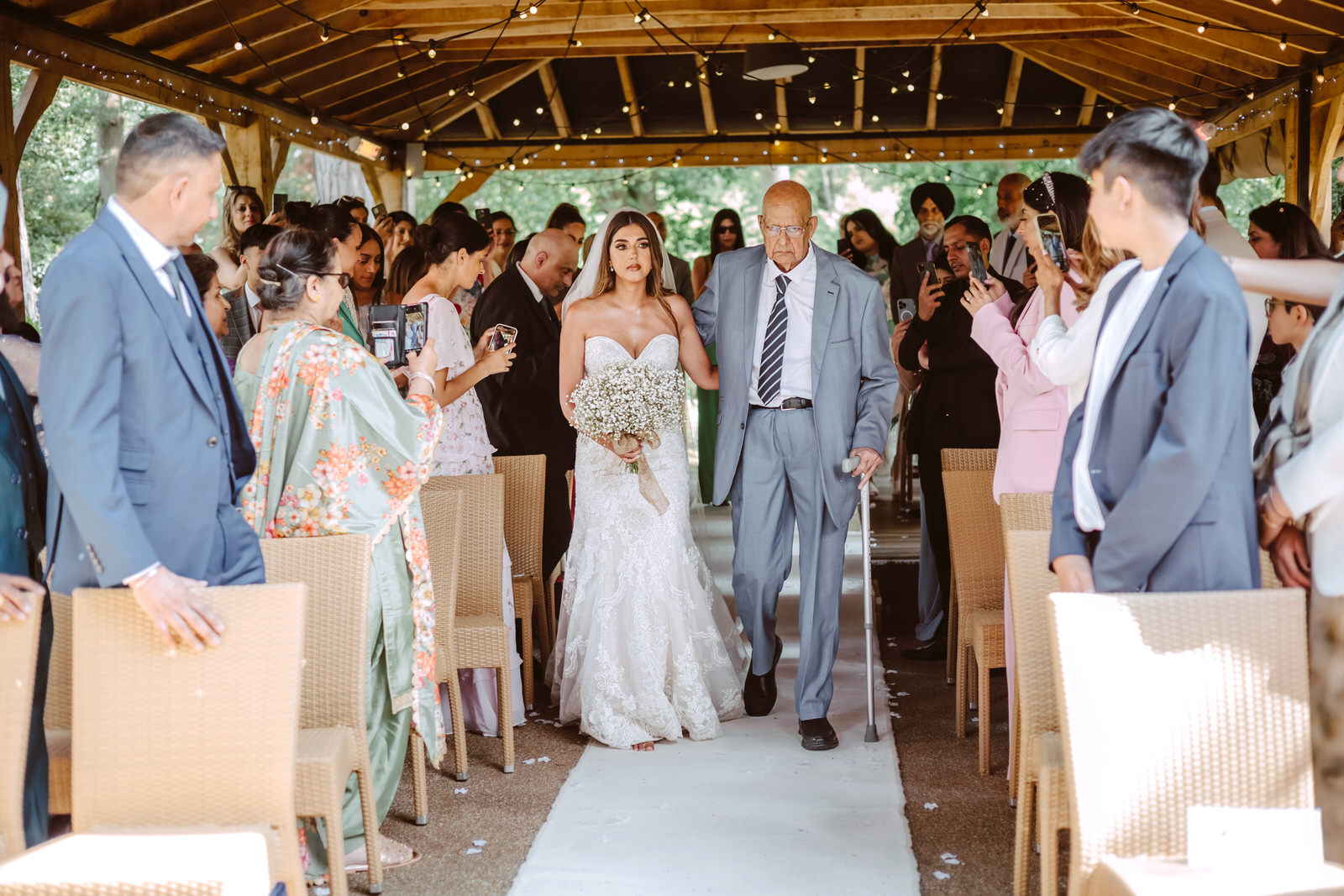 A bride and father of bride walking down the aisle in a gazebo.