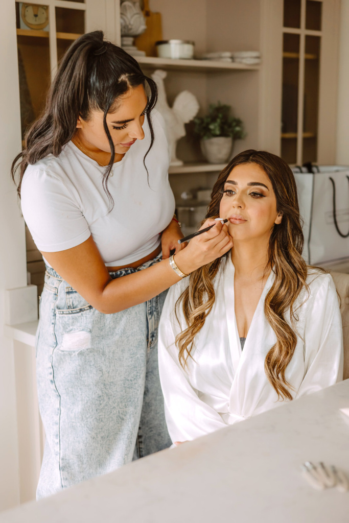 A bride is getting her makeup done by a makeup artist.