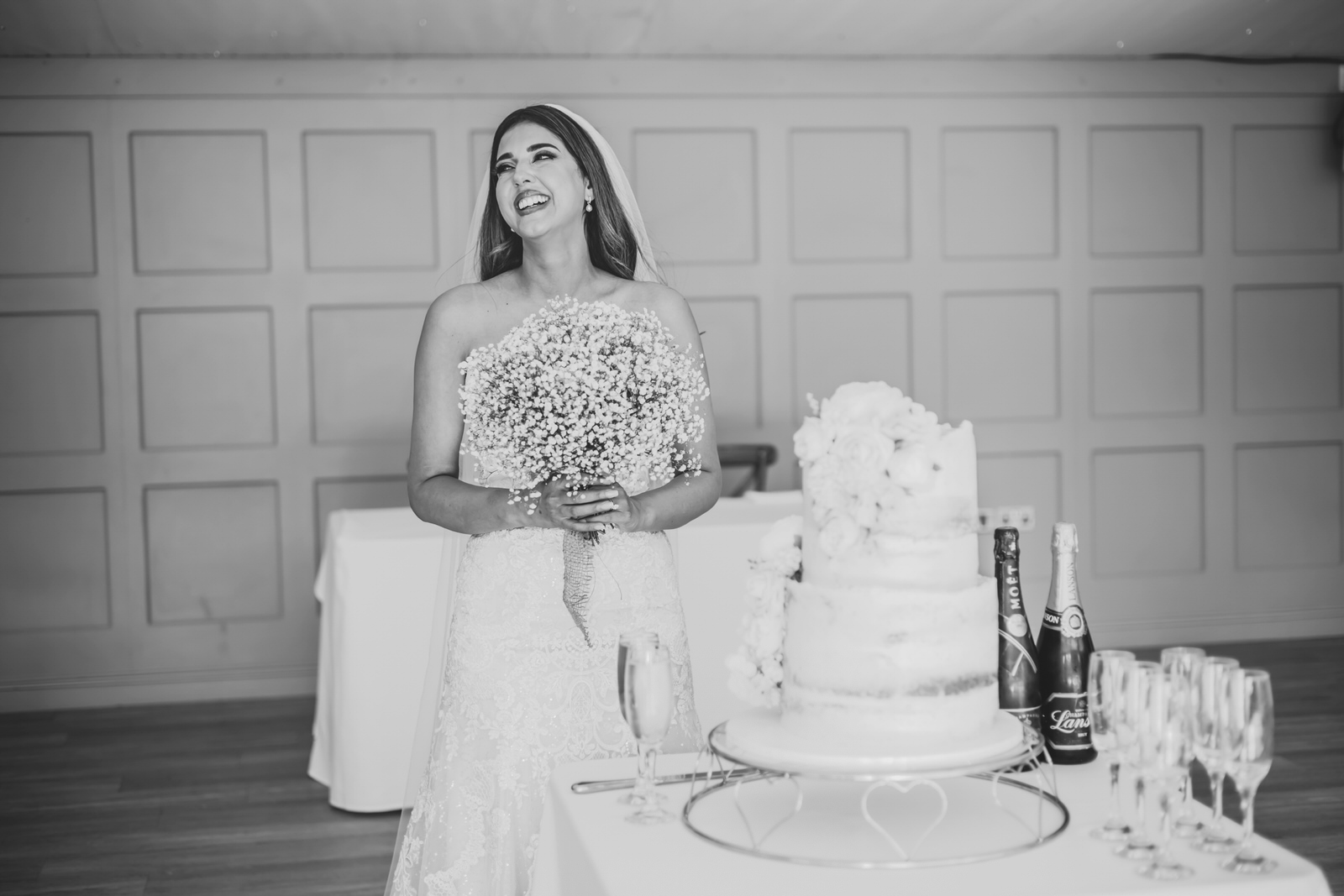 Black and white photo of a bride smiling at her wedding cake.
