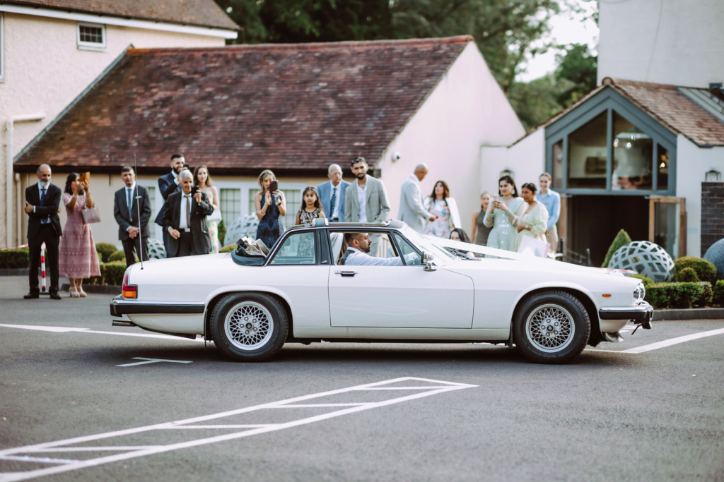 Bride and groom leave in a  white classic car from Hogarths Hotel car park. 