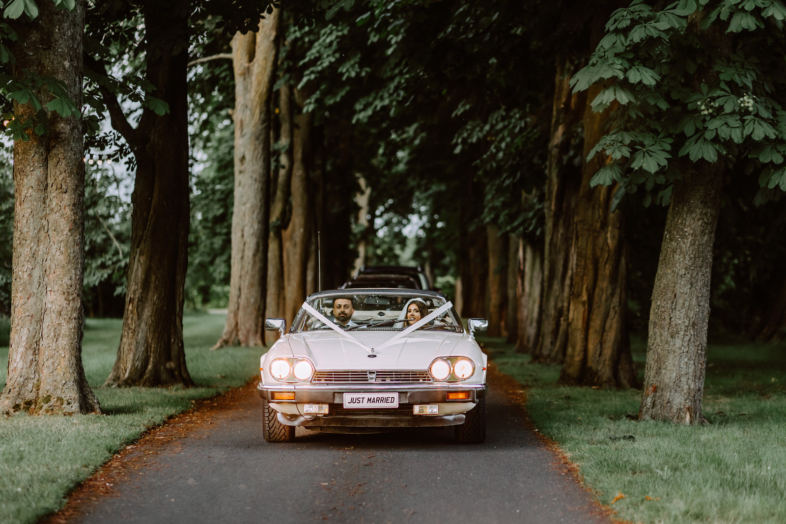 A wedding car is driving down a path in a wooded area.
