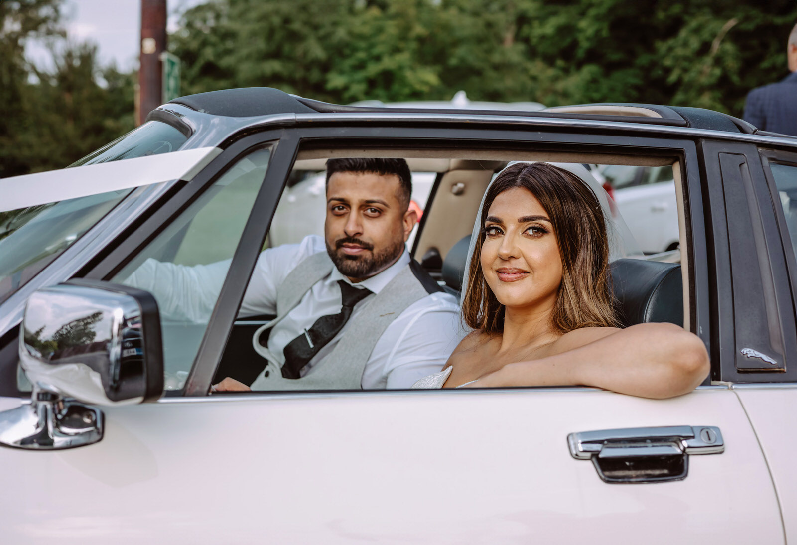 A bride and groom sitting in the back seat of a white car.