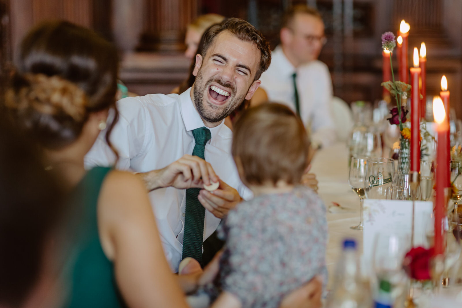 A man laughing at a dinner table with a child.