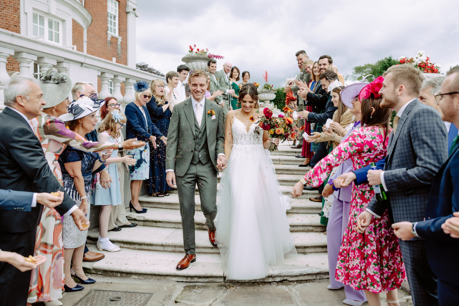 A bride and groom walking down the steps at a wedding. Guests throw confetti.