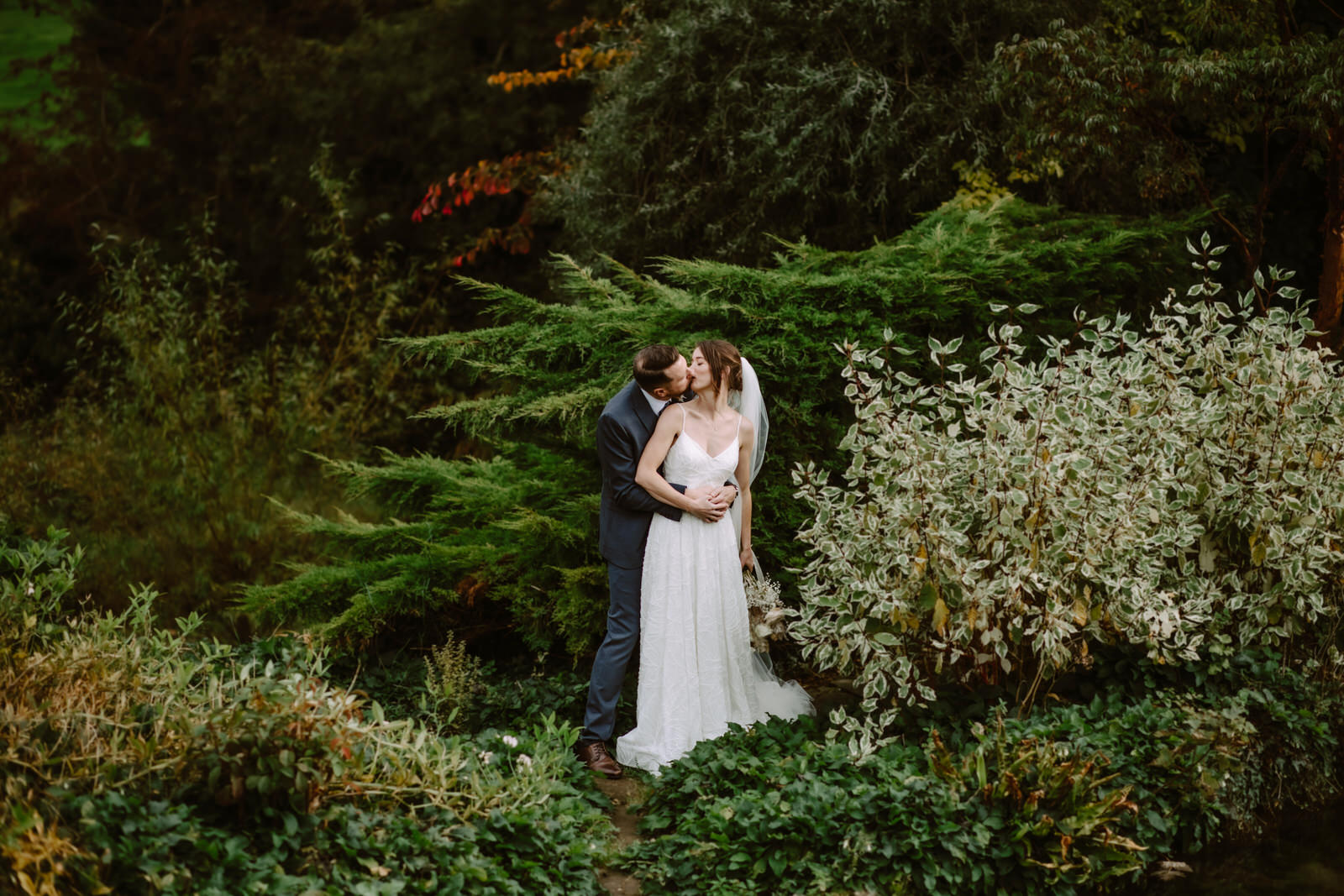 A bride and groom kissing in a garden.