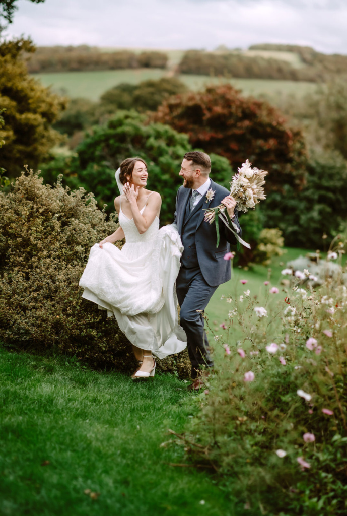 A bride and groom running through a garden.