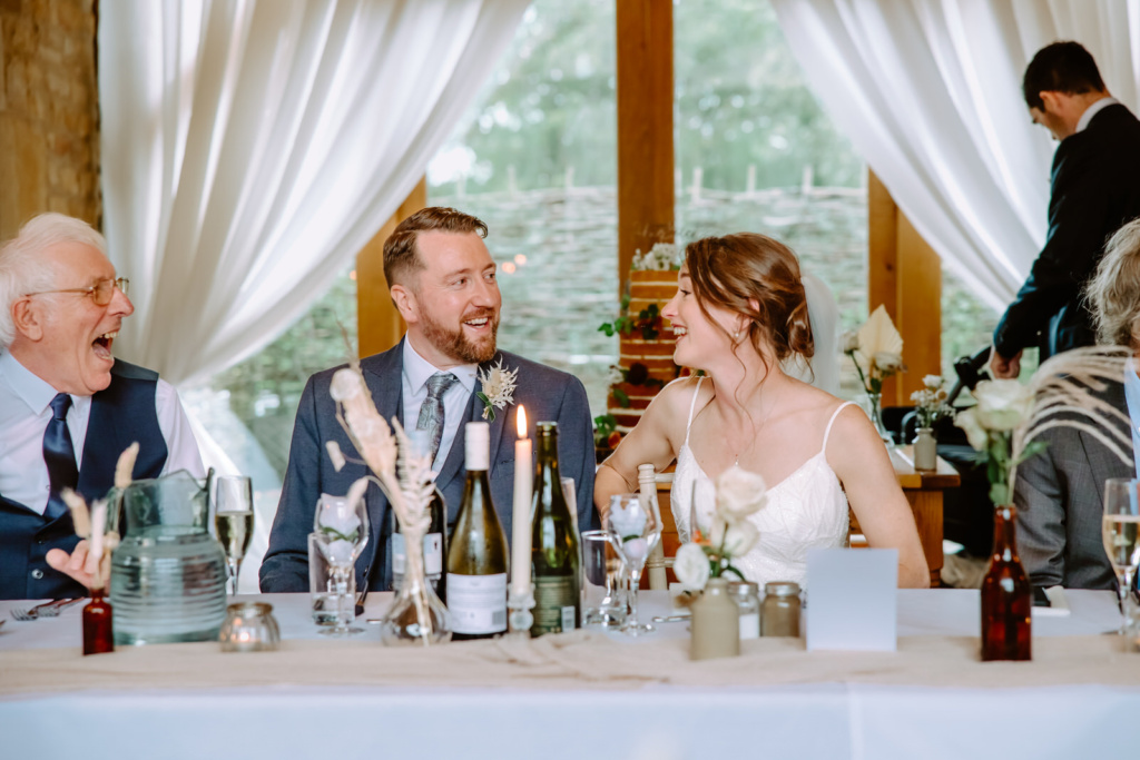 A bride and groom laughing at a table at a wedding reception.