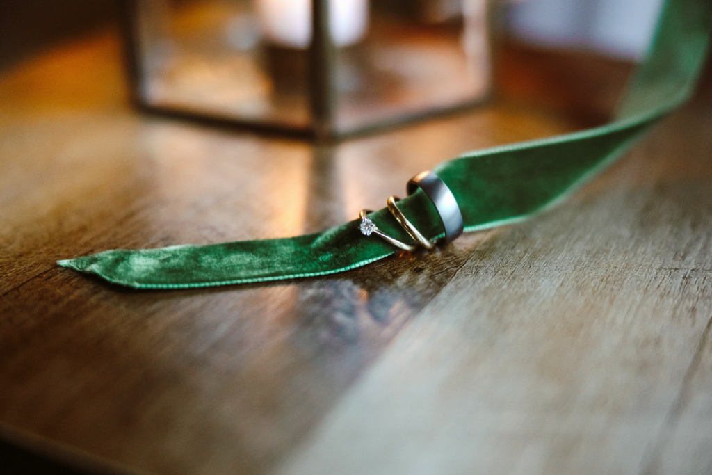 A green velvet ribbon sits on top of a wooden table with wedding rings.