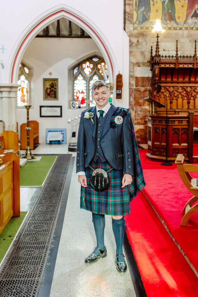 Agroom in a kilt standing in a church.