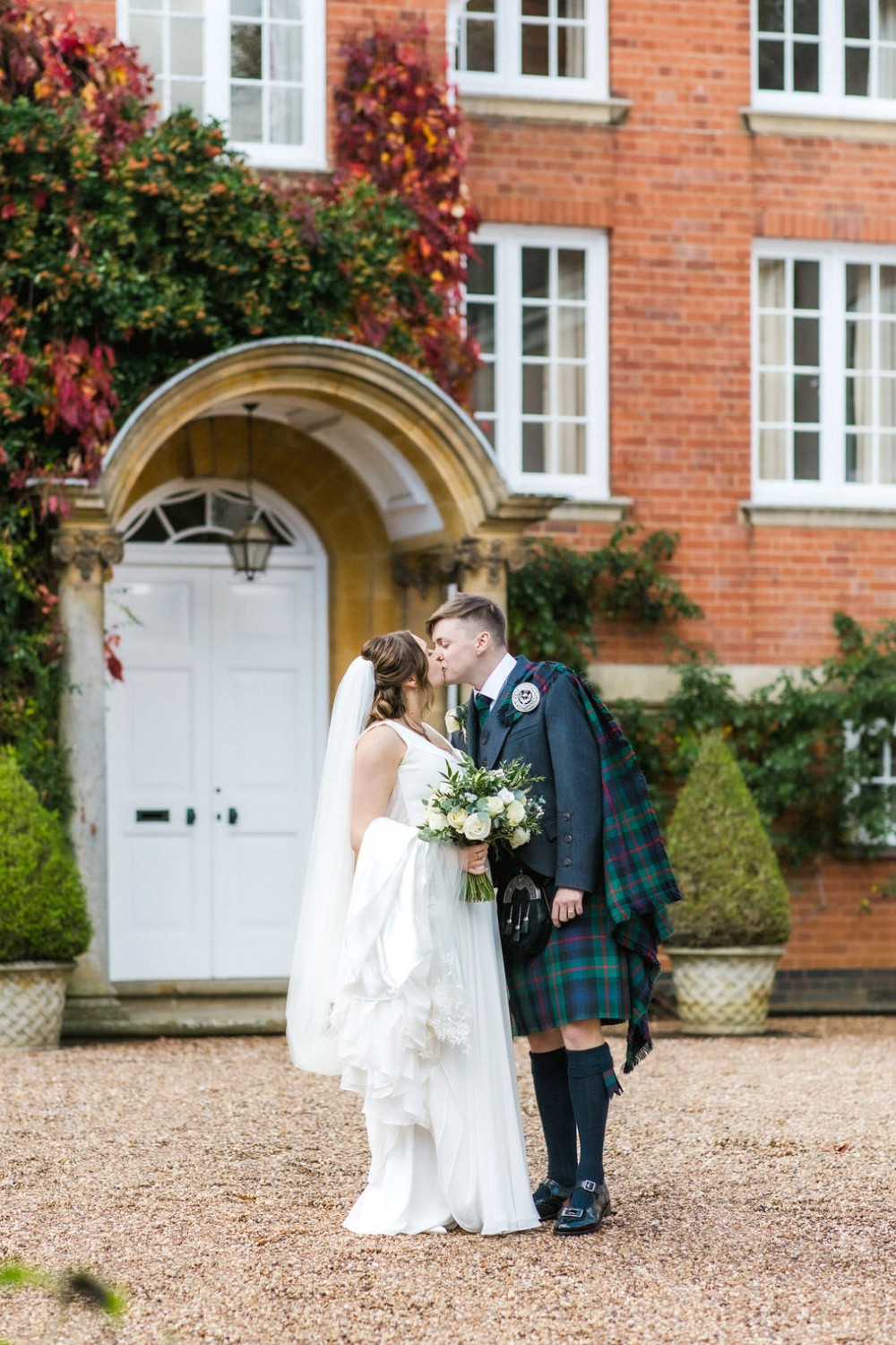 A bride and groom kissing in front of a red brick house.
