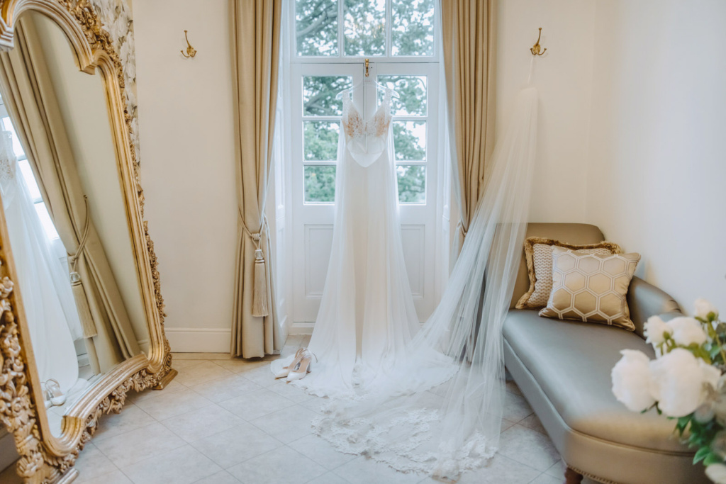 A wedding dress hangs in front of a mirror in The Lady Bourton Honeymoon Suite.