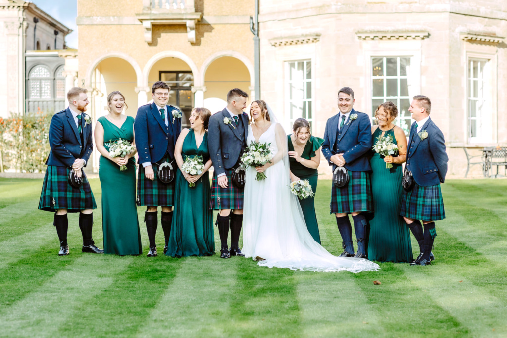 A wedding party in scottish kilts standing in front of a mansion.