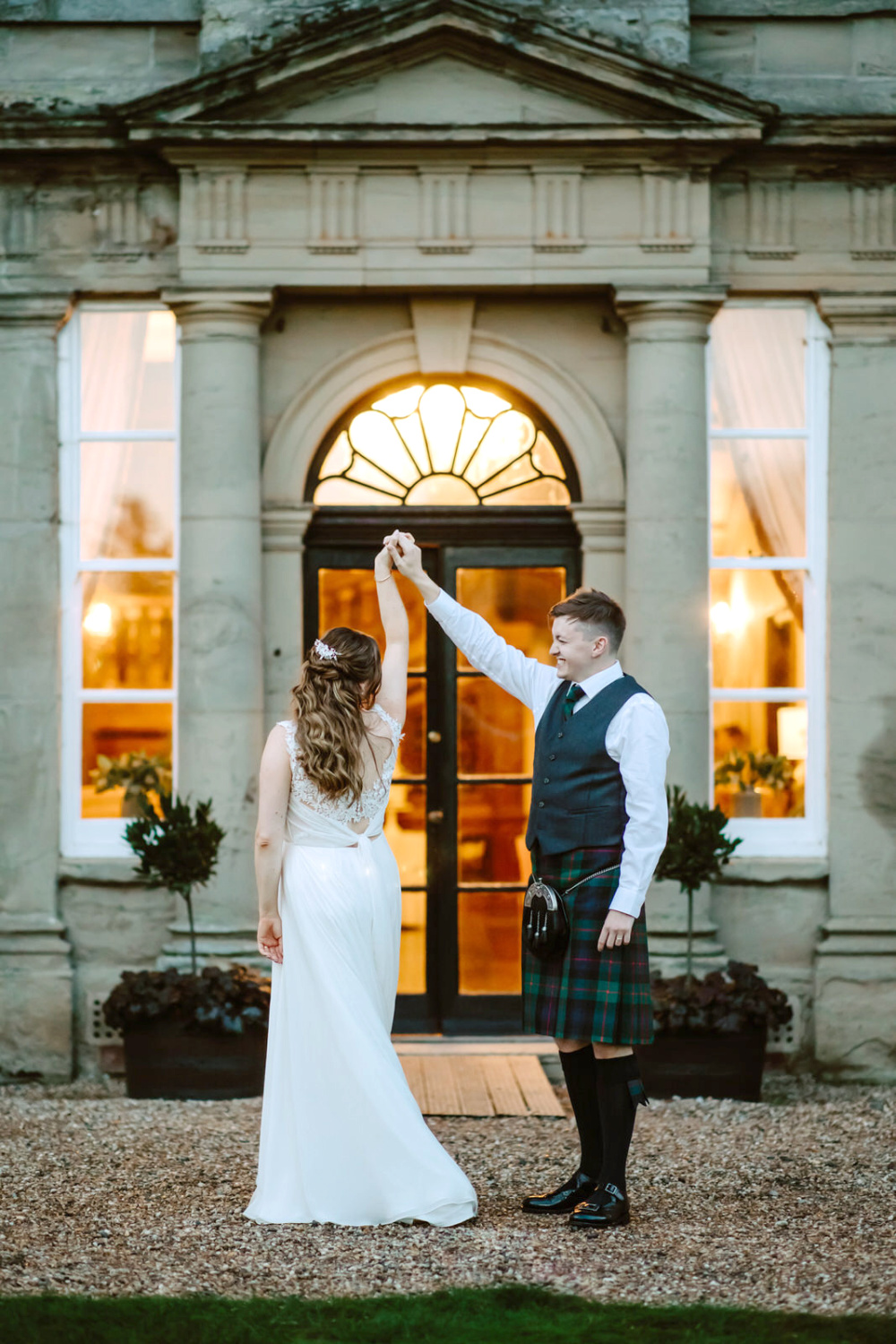 A bride and groom in kilts dancing in front of a Bourton Hall wedding
