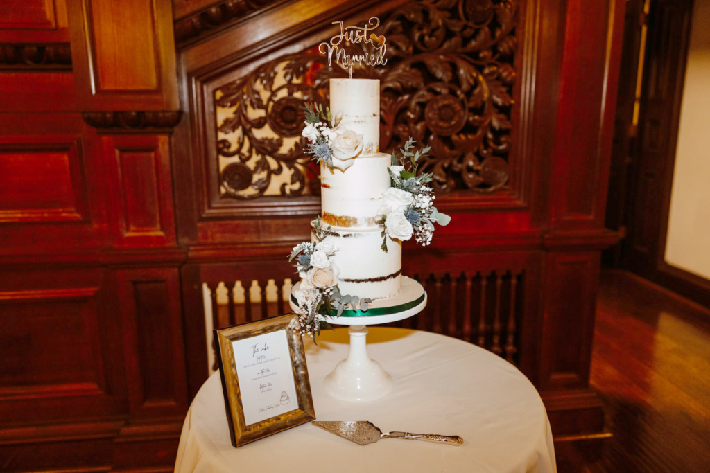 A wedding cake is sitting on a table in front of a staircase.