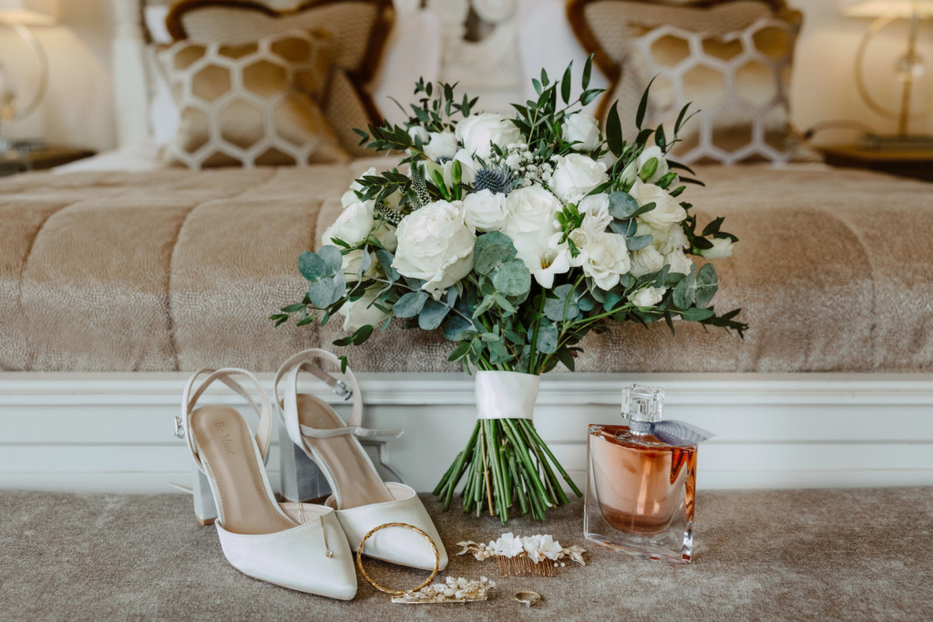 A bouquet of flowers and a pair of shoes on a bed.