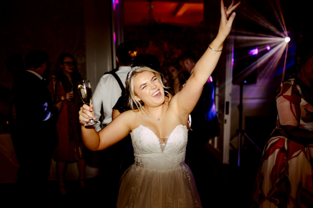 A bride in a wedding dress with her hands up in the air.