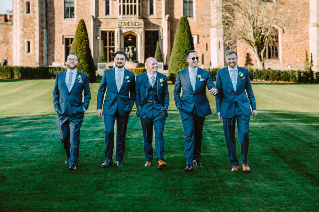 A group of groomsmen standing in front of a castle.