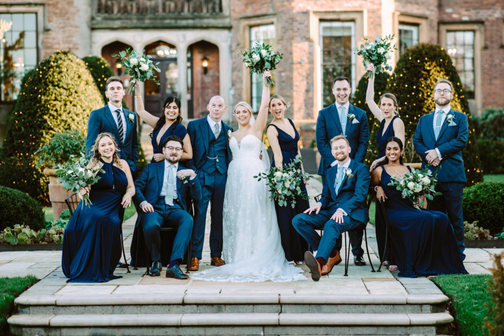 A group of bridesmaids and groomsmen pose for a photo in front of Rowton Castle.
