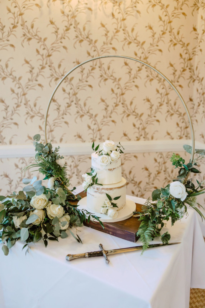 A wedding cake on a table with greenery and a sword.