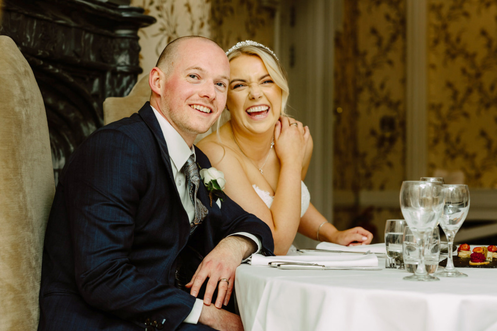A bride and groom smiling at each other at a table.