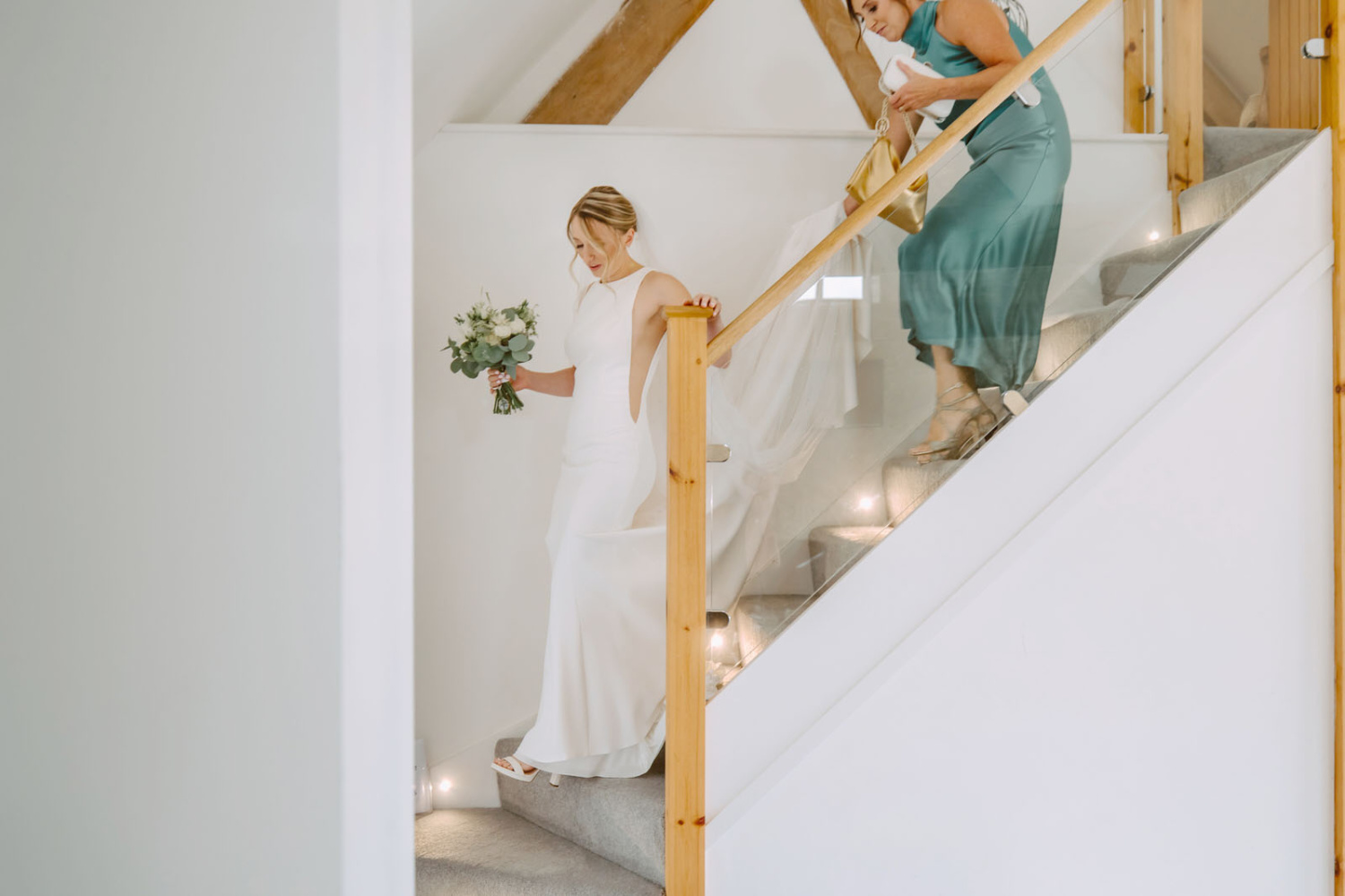 The bride and her mum walking down the stairs in a wedding dress.