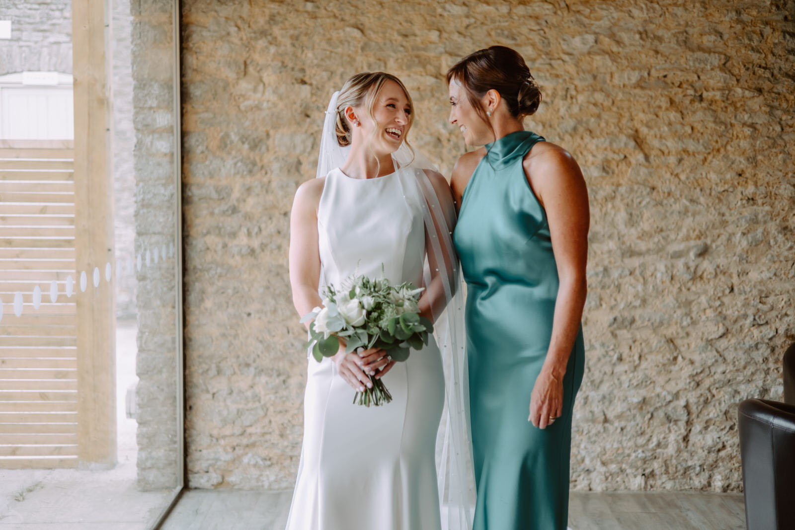 Two bridesmaids standing in front of a stone wall.