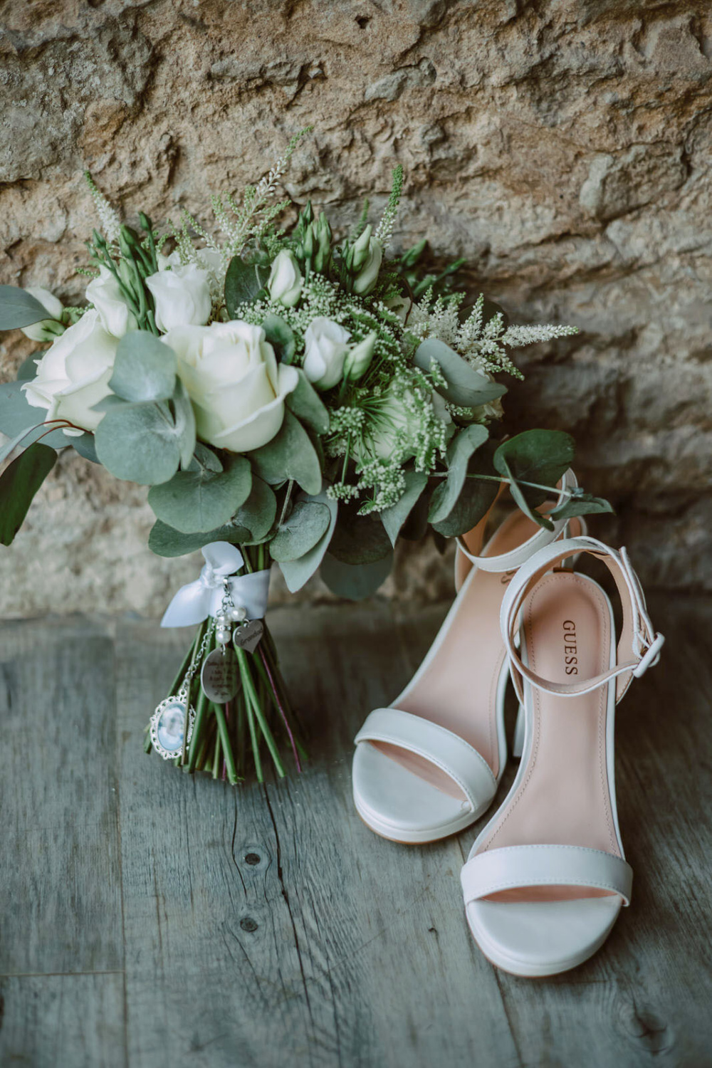 White wedding shoes and bouquet on a wooden table.
