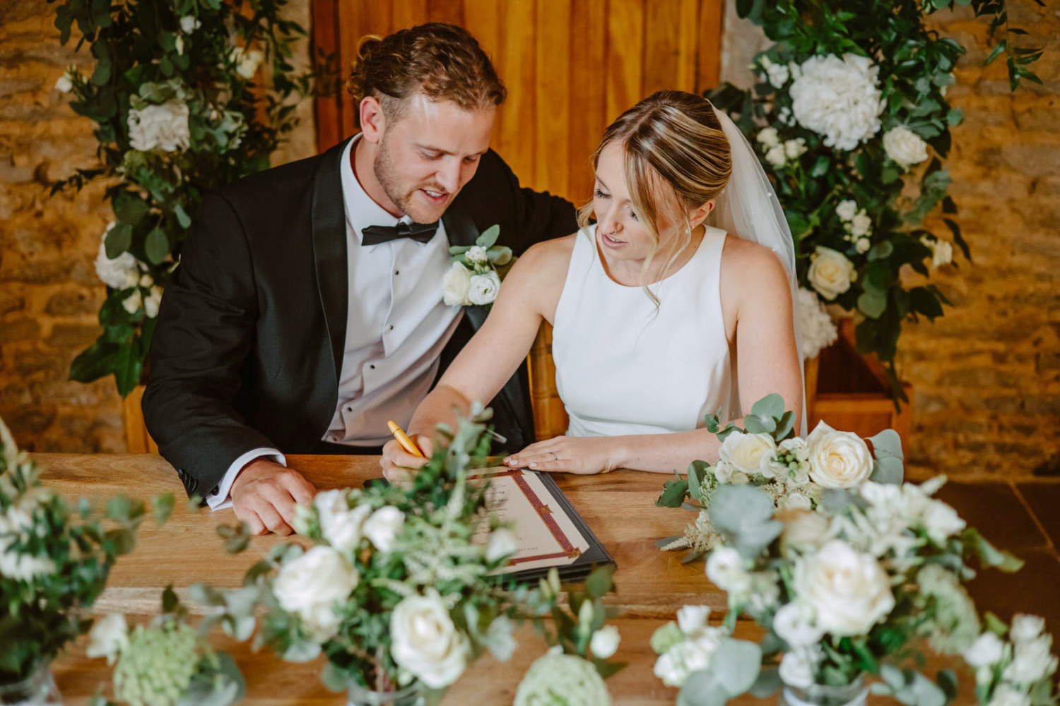 A bride and groom signing their wedding vows at a table at Stratton Court Barn.
